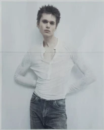 Young model with spiky hair wearing a white henley shirt and denim jeans against a pale grey seamless background.