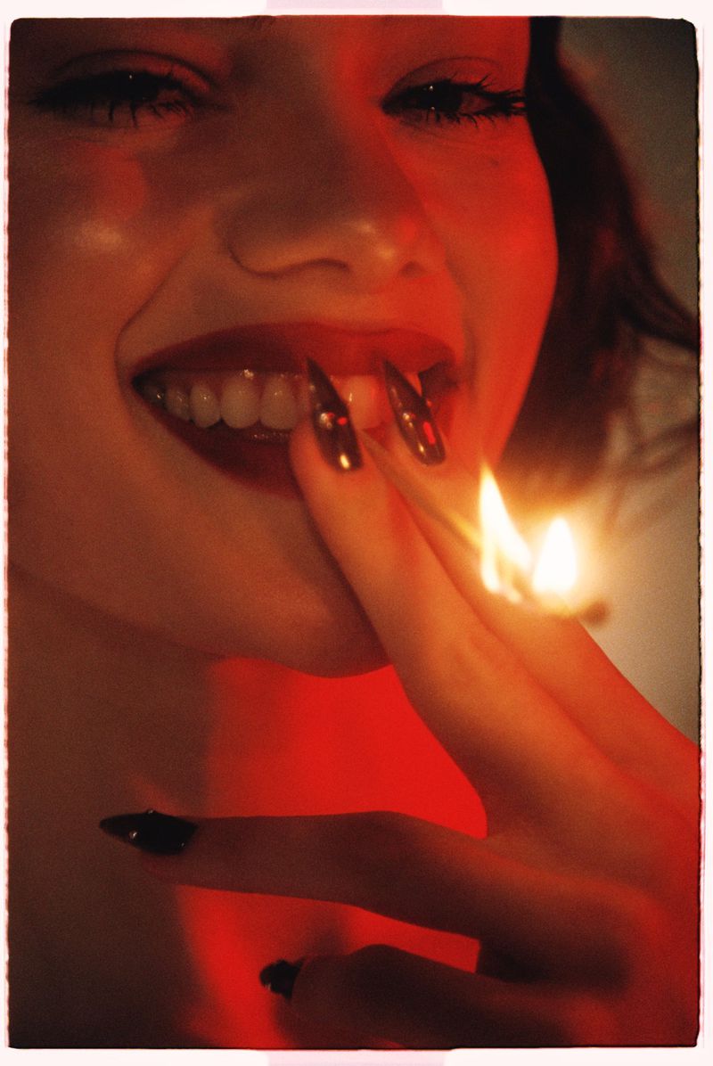 Close-up portrait of a smiling woman holding a burning match near her face in red light