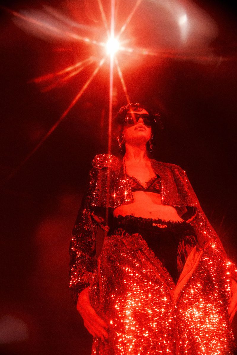 Low-angle shot of a model wearing a glittering red sequined coat and dark sunglasses under a dramatic starburst light source