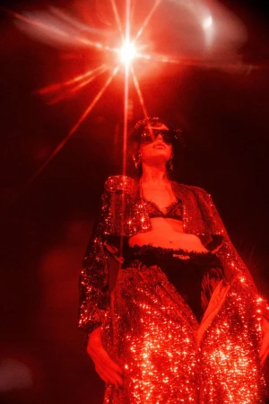 Low-angle shot of a model wearing a glittering red sequined coat and dark sunglasses under a dramatic starburst light source
