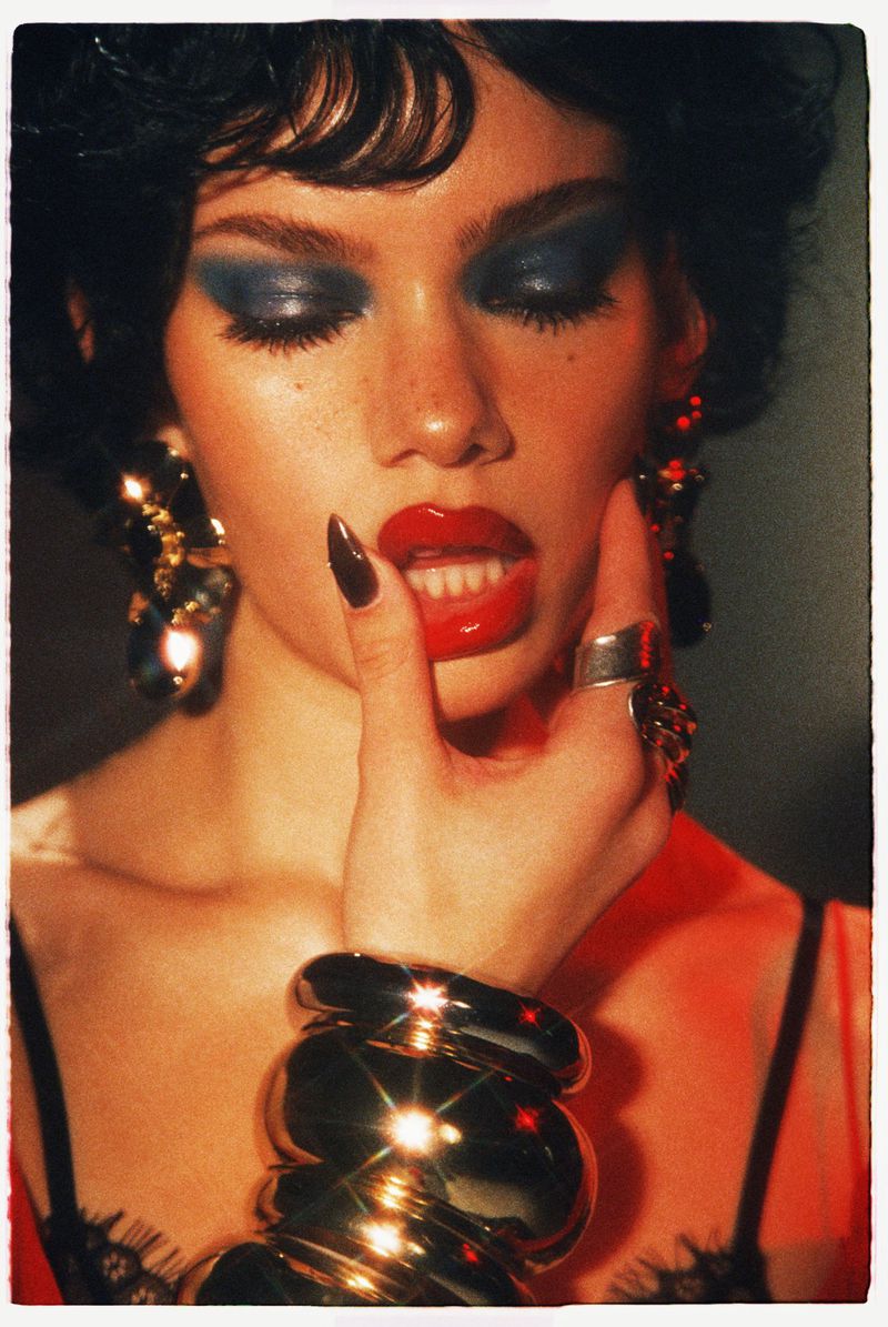 Close-up portrait of a woman with bold blue eyeshadow, red glossy lips, chunky silver cuffs, and oversized earrings by Benjo Arwas.