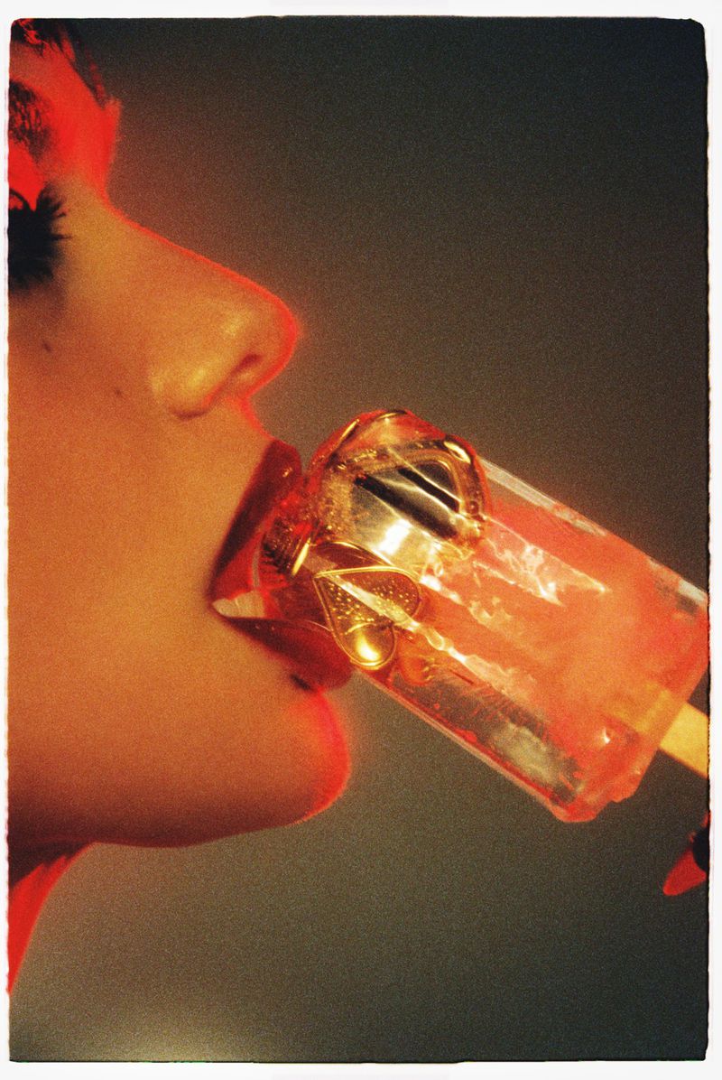 Close-up profile of a woman biting into a translucent red ice pop containing gold charms, shot by Benjo Arwas for Numero Netherlands.