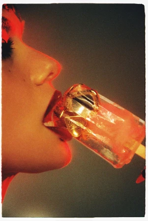 Close-up profile of a woman biting into a translucent red ice pop containing gold charms, shot by Benjo Arwas for Numero Netherlands.