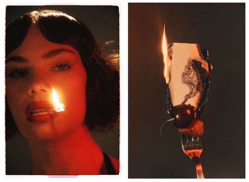 Close-up of a woman with dark hair holding a lit match near her lips, paired with a burning playing card on a fork.