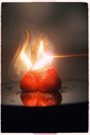Two strawberries lit on fire with visible flames and smoke against a dark background, captured by Benjo Arwas for Numero Netherlands.