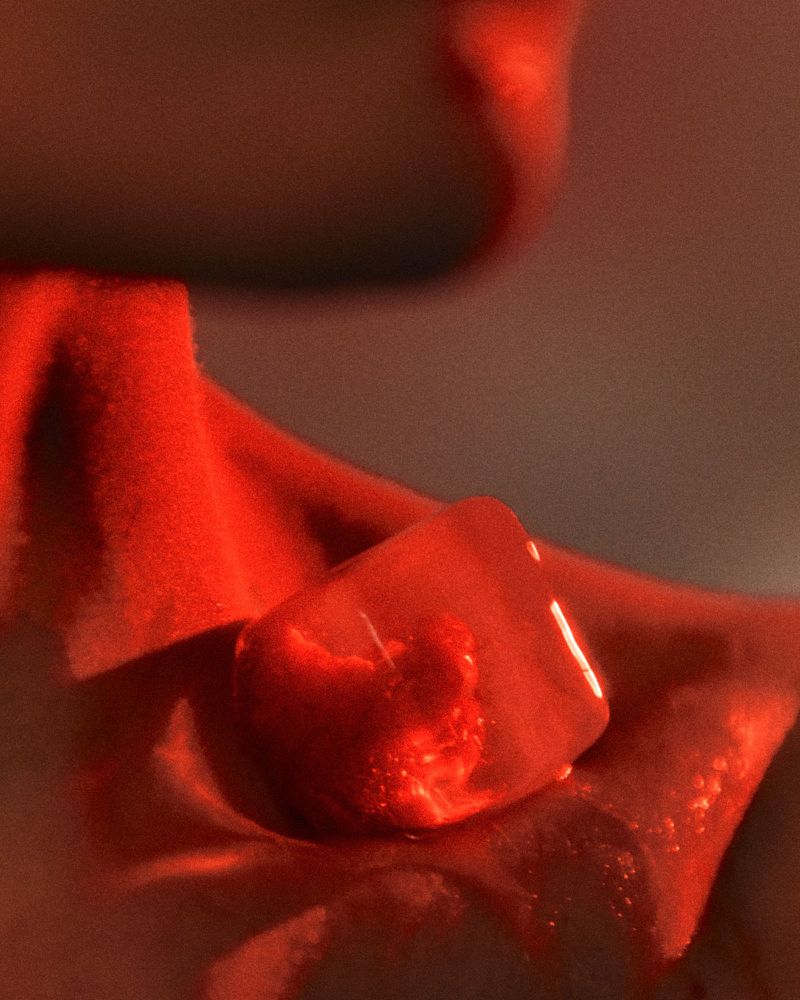 Close-up of a melting ice cube resting against fabric under dramatic warm red lighting, shot by Benjo Arwas.