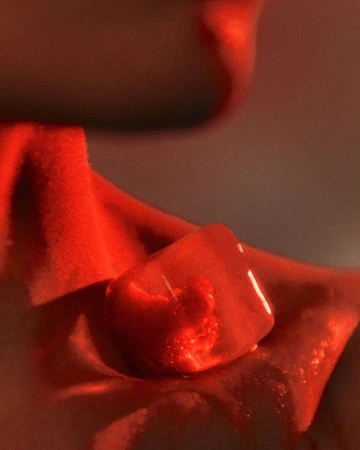 Close-up of a melting ice cube resting against fabric under dramatic warm red lighting, shot by Benjo Arwas.