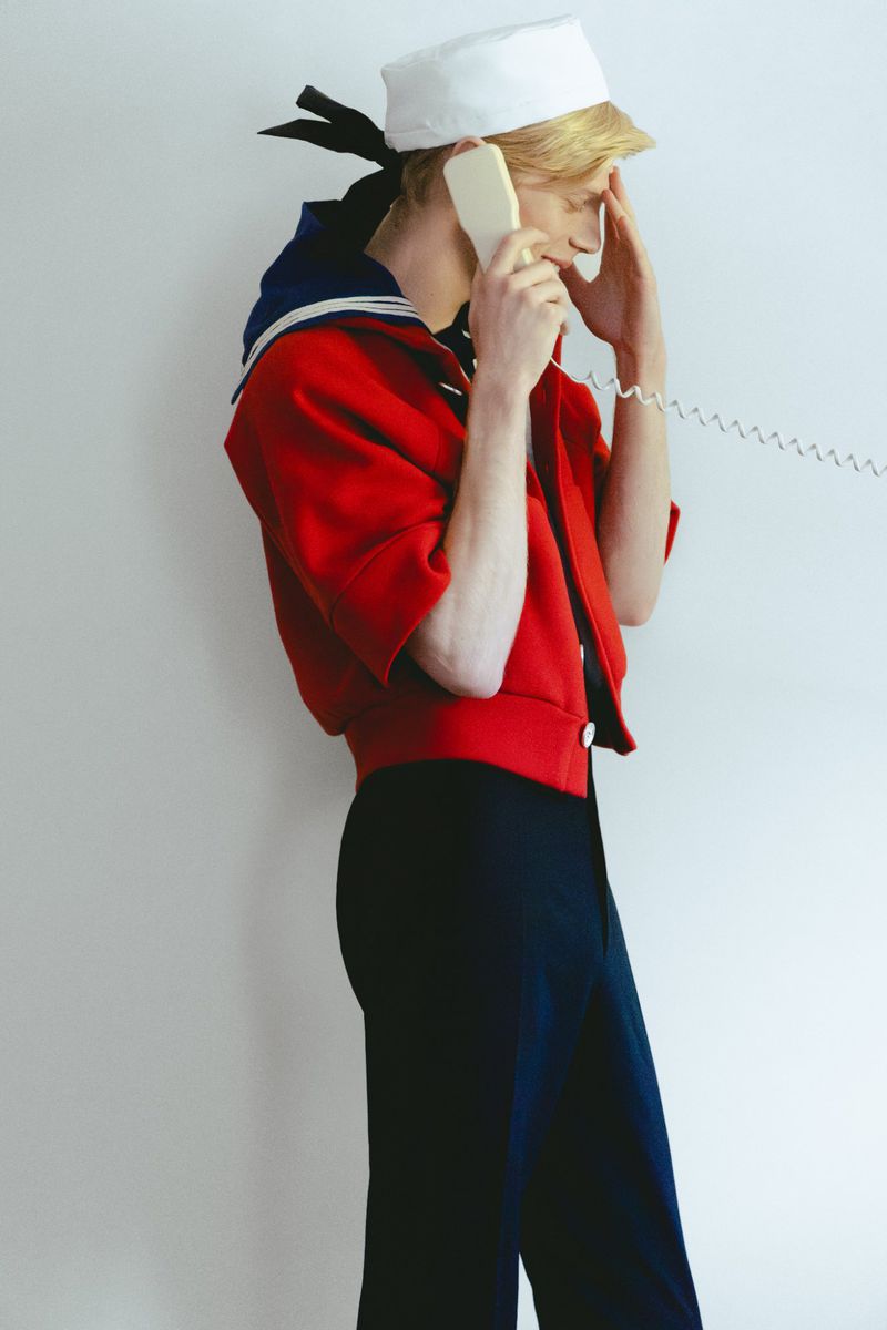Model wearing a sailor-inspired red jacket and white cap holding a telephone receiver against a plain white background.