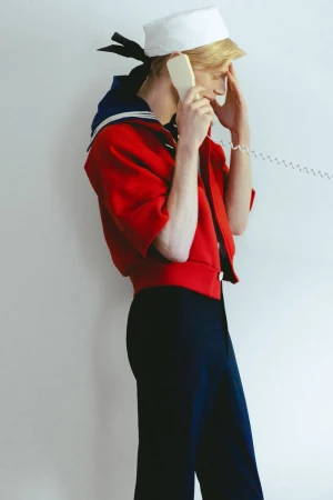 Model wearing a sailor-inspired red jacket and white cap holding a telephone receiver against a plain white background.