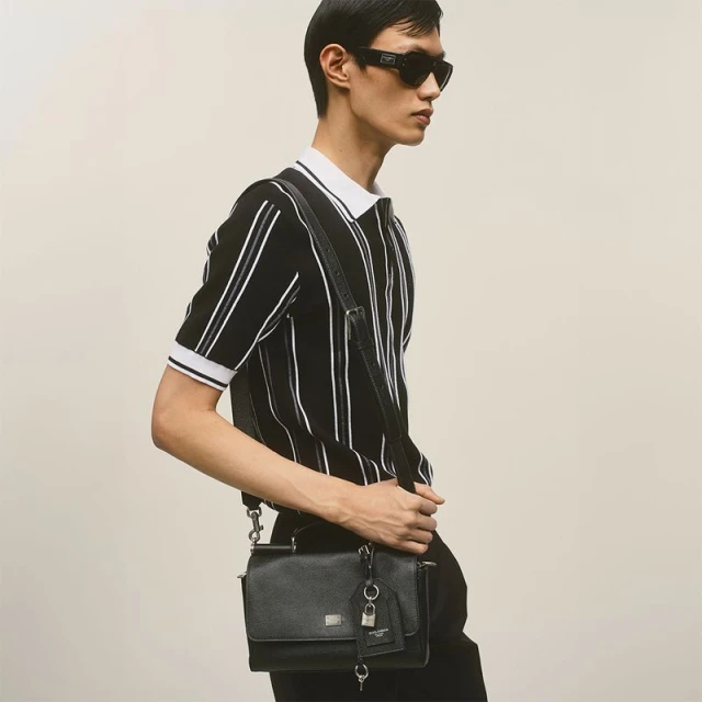 Model wearing a black and white striped polo shirt and black sunglasses with a black leather crossbody bag.