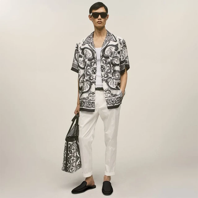 East Asian male model wearing black and white printed shirt, white trousers, sunglasses, and holding a matching patterned tote bag.