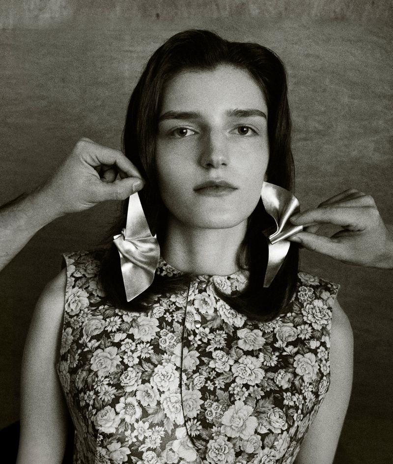 Portrait of a woman wearing a floral dress with two hands adjusting sculptural silver earrings in her ears.