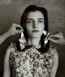 Portrait of a woman wearing a floral dress with two hands adjusting sculptural silver earrings in her ears.
