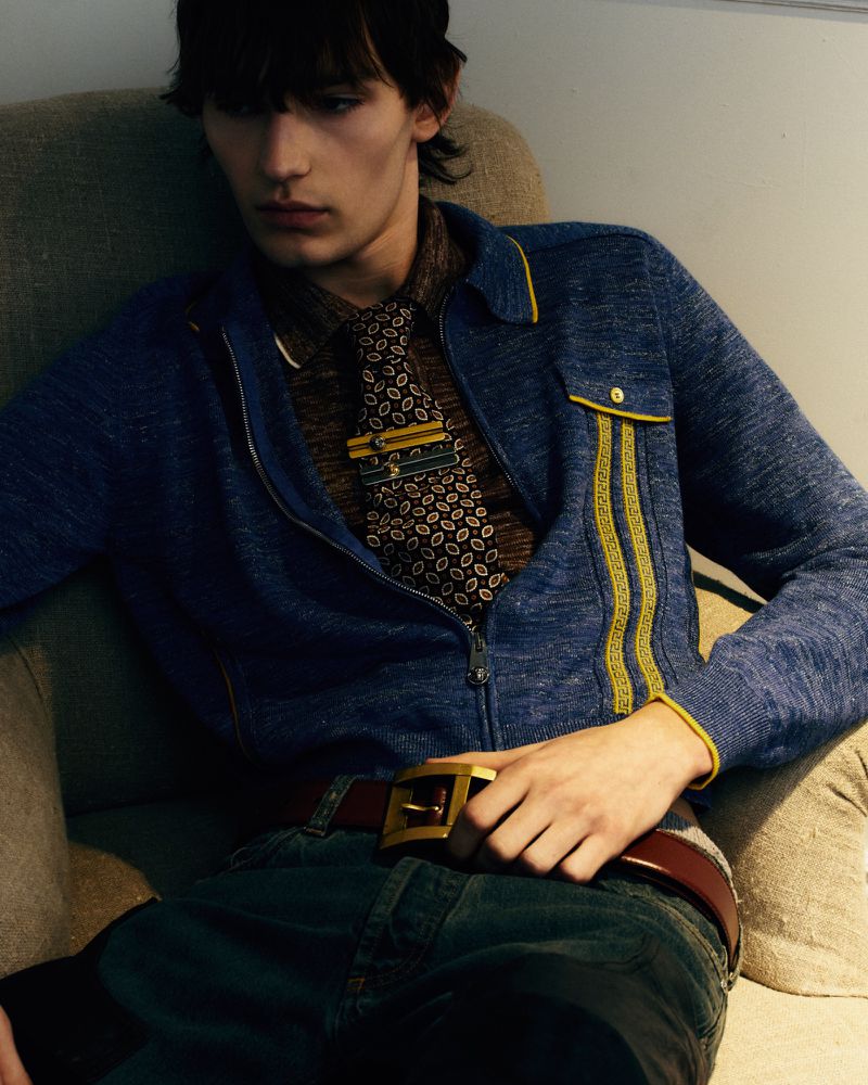 Young man wearing a blue zip-up jacket and patterned tie seated on an armchair for YUNG Magazine.
