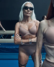 Elderly woman wearing nude lingerie and dark sunglasses with arms crossed inside a gym