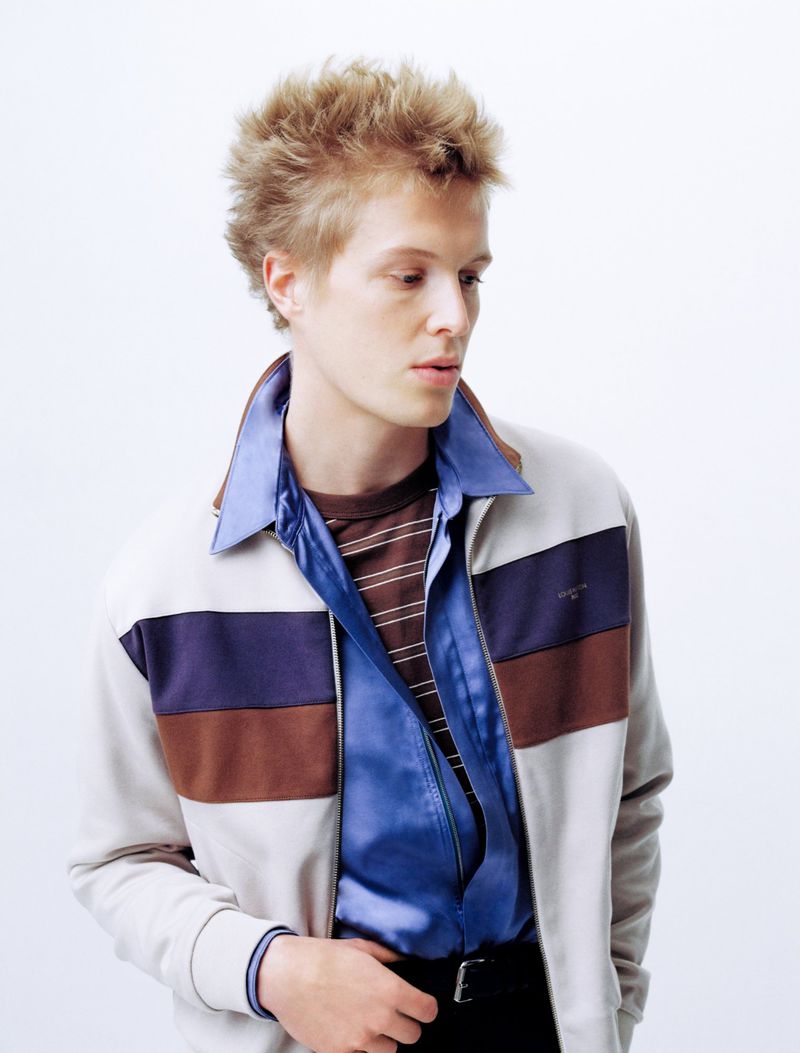 Portrait of young blond man in striped jacket and blue satin shirt against a white seamless background