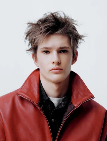 Young male model with messy hair wearing a red leather jacket over dark layers against a plain white background