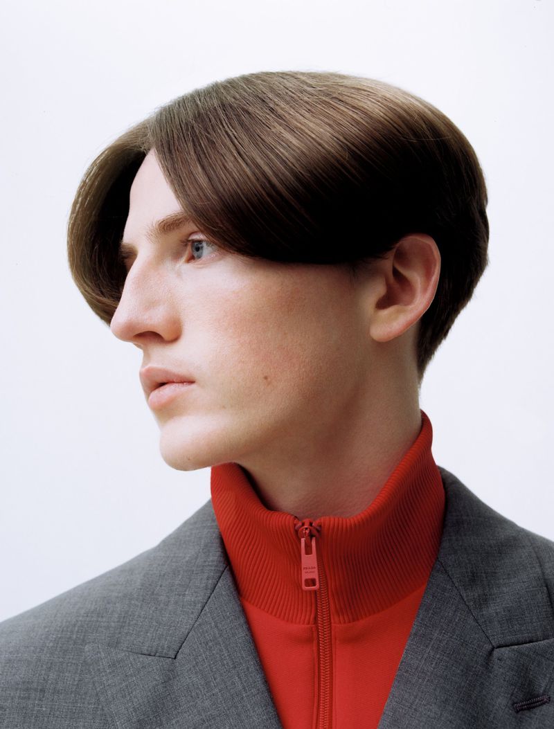 Portrait of a man wearing a grey jacket over a red zip-up top against a white background