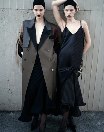 Two female models in dark attire posing against a textured concrete wall for Vogue Adria editorial