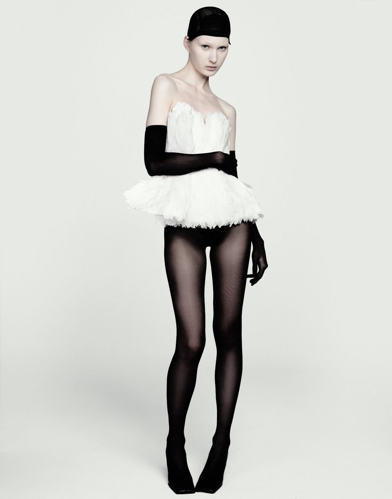 Model in white strapless ruffled top with black opera gloves and tights against plain white backdrop