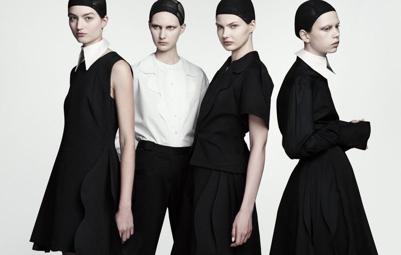 Four female models wearing black and white monochrome outfits with hair nets against a plain white seamless backdrop