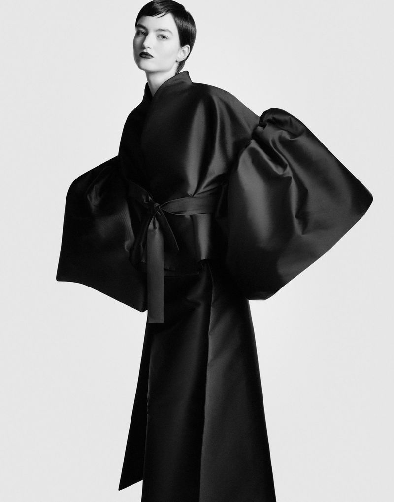 Model wearing voluminous black sculptural jacket with exaggerated sleeves against a white background