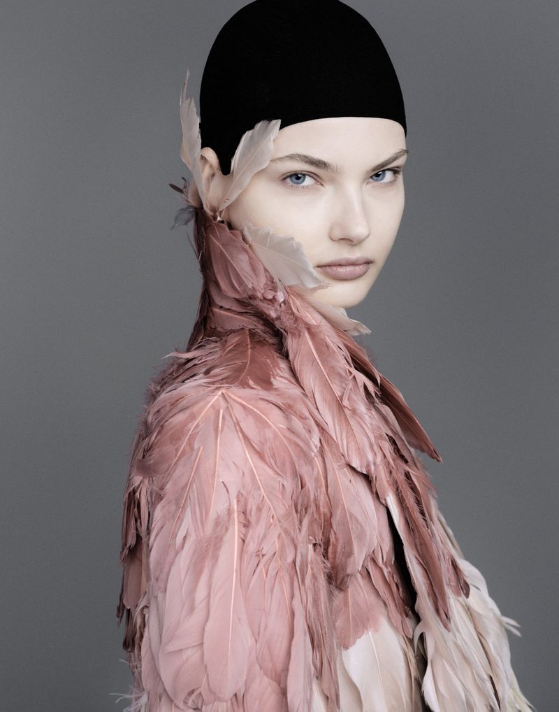 Model wearing a pink feathered collar and black cap against a grey background for Vogue Adria