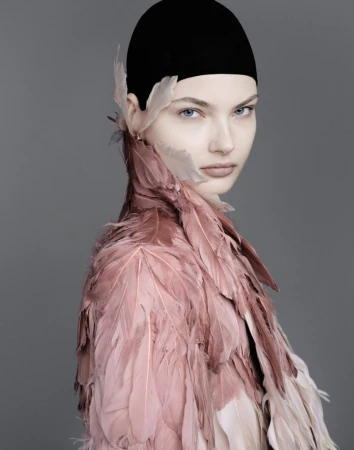 Model wearing a pink feathered collar and black cap against a grey background for Vogue Adria