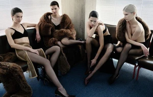 Four female models seated on dark leather sofas in a room with white window blinds, wearing black bras and fur stoles for Vogue Adria.