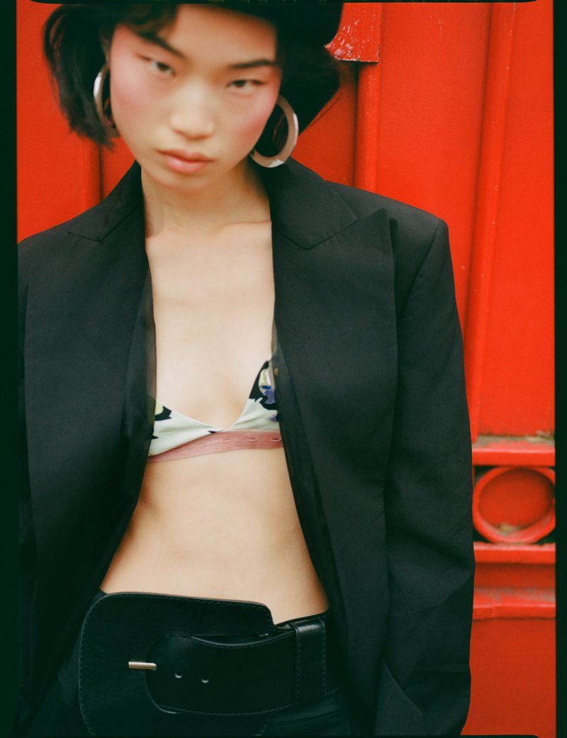 Model in black blazer and large silver hoop earrings against vibrant red wall background