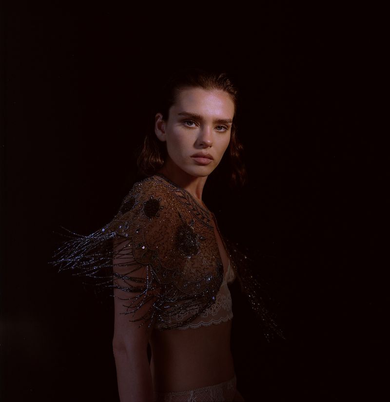 Portrait of a woman wearing a beaded fringe top against a dark, low-key background photographed by Soraya and Rodrigo.