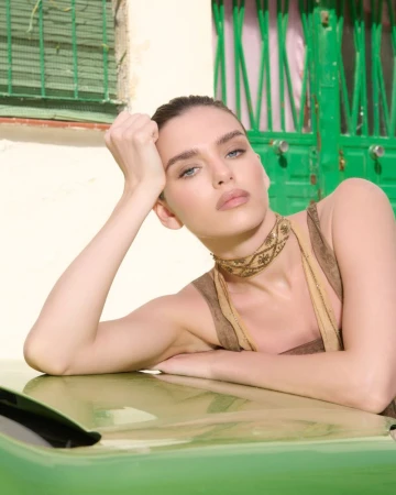 Woman resting her chin on her hand, leaning on a green vehicle with a matching green door and pale wall in the background.