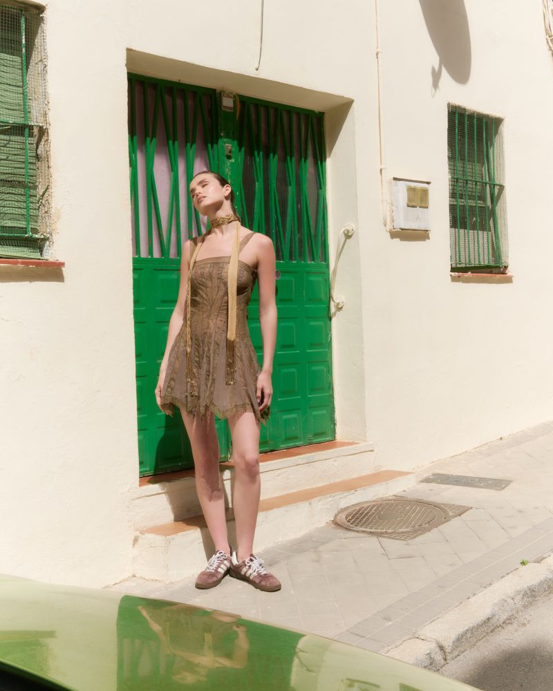 Woman in patterned dress and sneakers standing outside a building with green doors for Vika K.