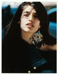 Portrait of a woman wearing an ornate metal earring with blue stones and a dark textured top outdoors in natural light