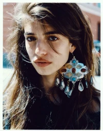 Close-up portrait of a woman with long dark hair wearing large ornate silver earrings with turquoise stones for Cala by Johnson Lui