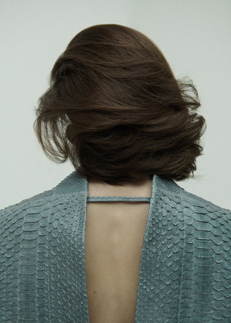 Back view of a woman with brown hair wearing a textured blue garment against a plain light background