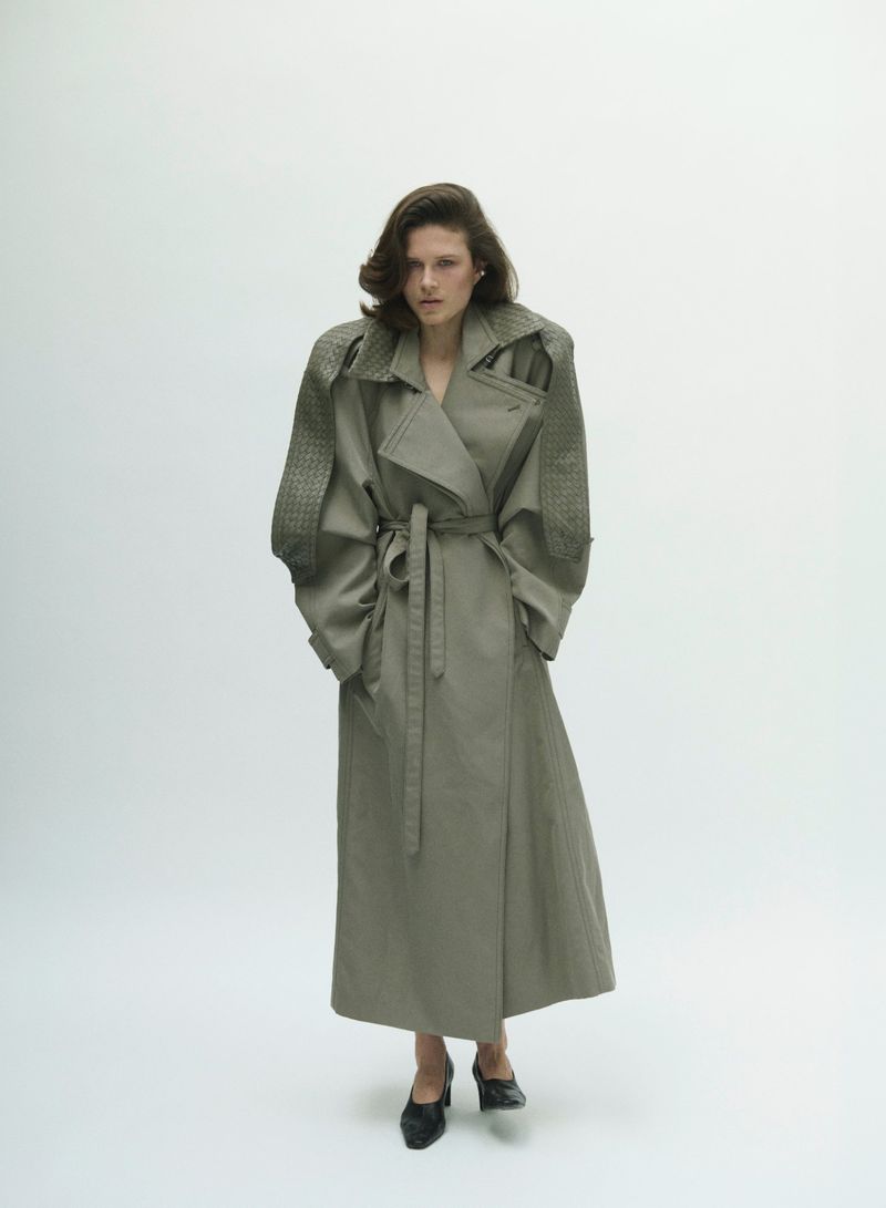 Model Lonneke Te Kloese wearing a grey belted trench coat against a white seamless background for Puss Puss Magazine.