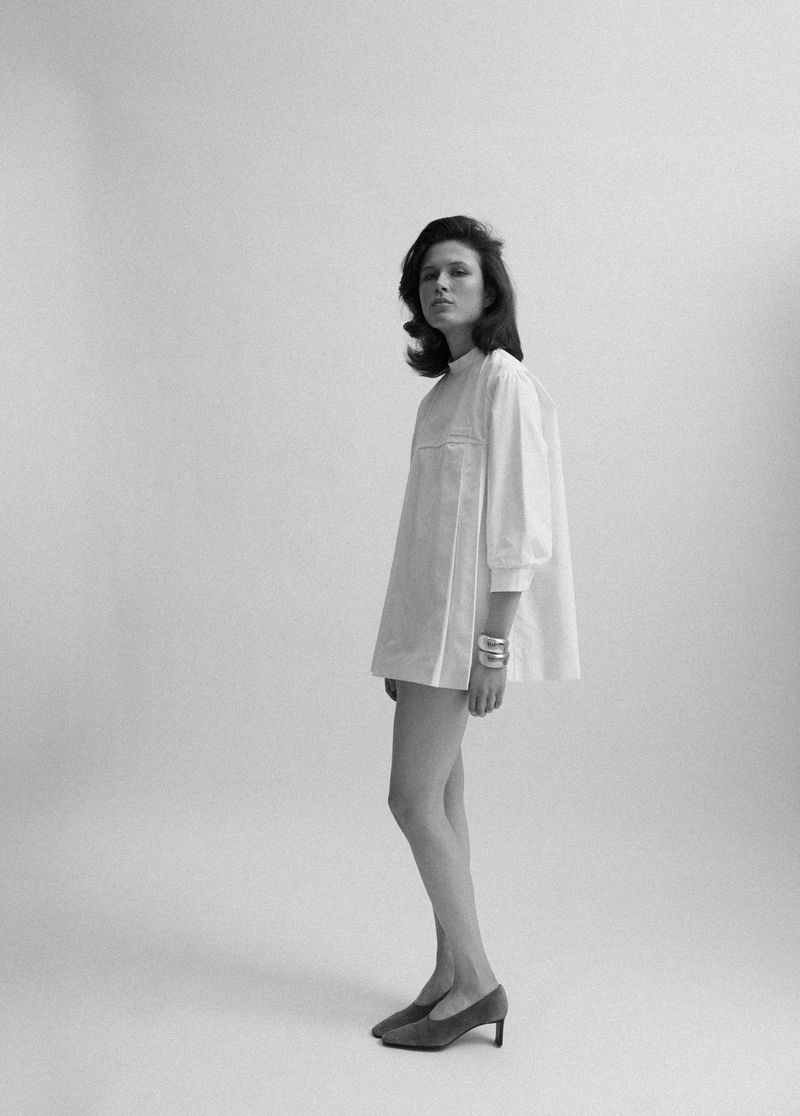Model Lonneke Te Kloese in a white tunic dress and dark heels against a white studio background for Puss Puss Magazine