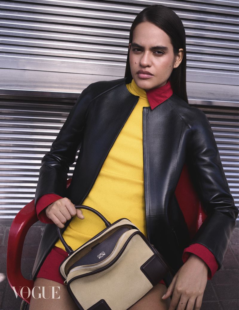 Model wearing a black leather jacket, yellow top, and red collar seated with a handbag, Vogue Arabia Bright Future project