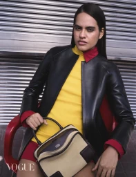Model wearing a black leather jacket, yellow top, and red collar seated with a handbag, Vogue Arabia Bright Future project