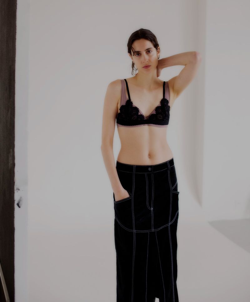 Model in black floral bra and dark skirt posing against a neutral white wall for WRPD Magazine.