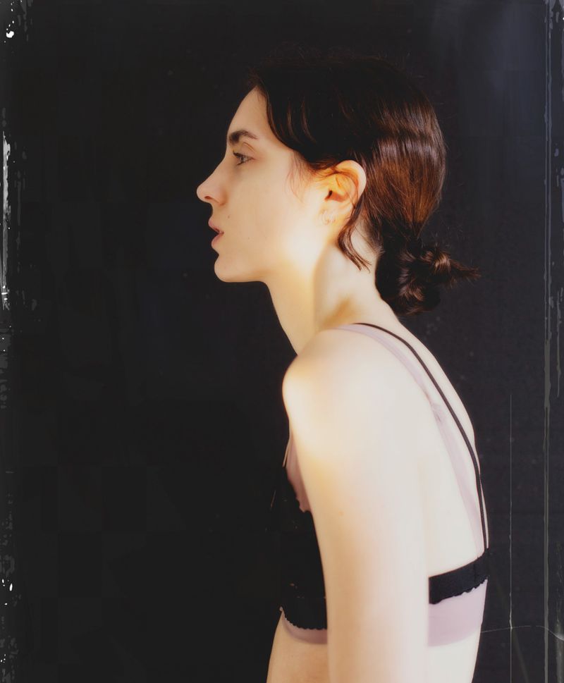 Profile portrait of a young female model in dark underwear against a black background shot on analogue film
