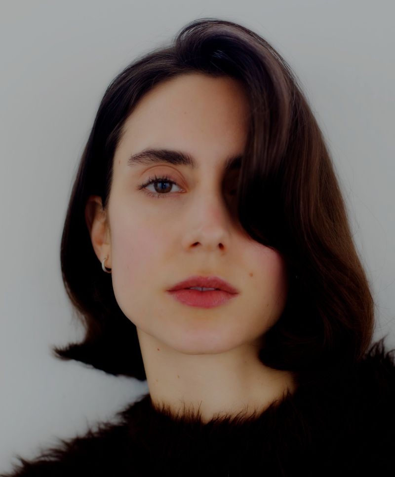 Close-up portrait of a woman with dark short hair and a black textured top against a plain white background