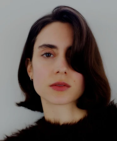 Close-up portrait of a woman with dark short hair and a black textured top against a plain white background