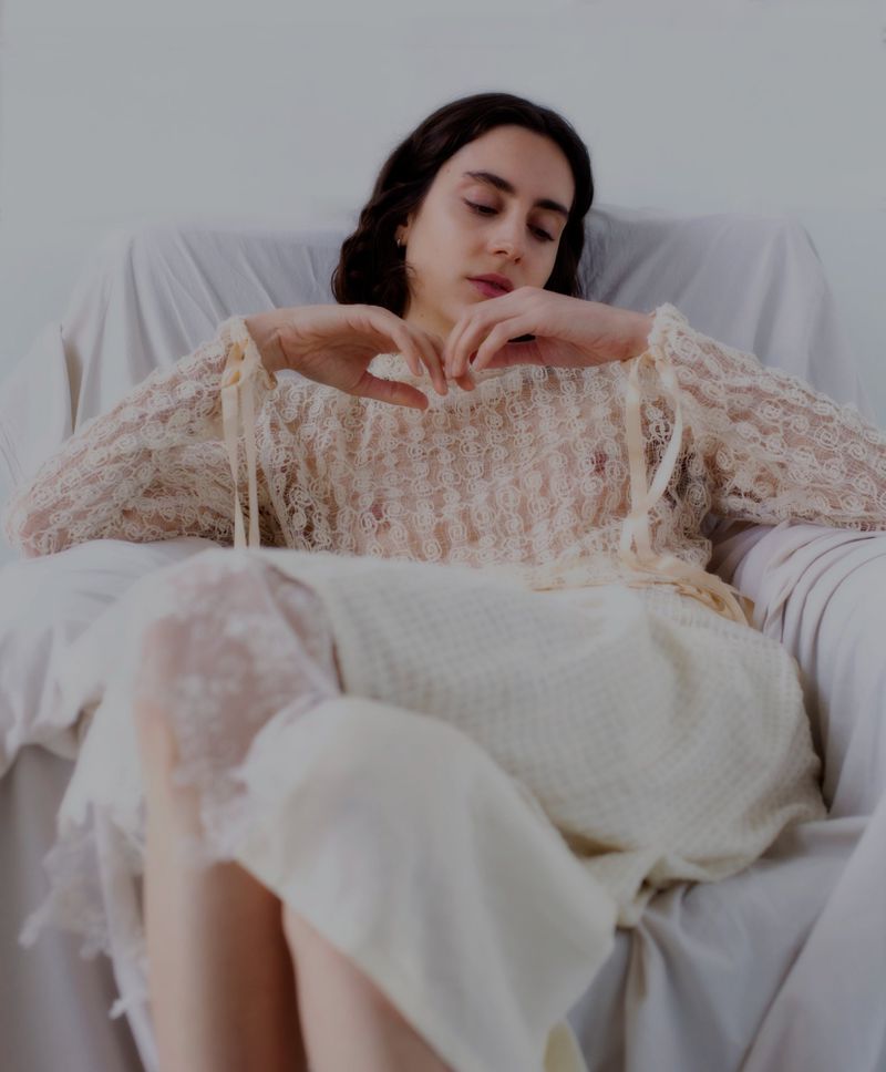 Model seated in an armchair wearing a sheer lace top and light skirt for WRPD Magazine