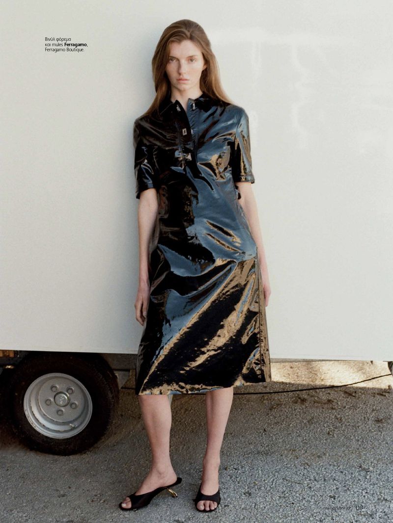 Model in shiny black leather dress standing against a plain white wall next to a vehicle wheel