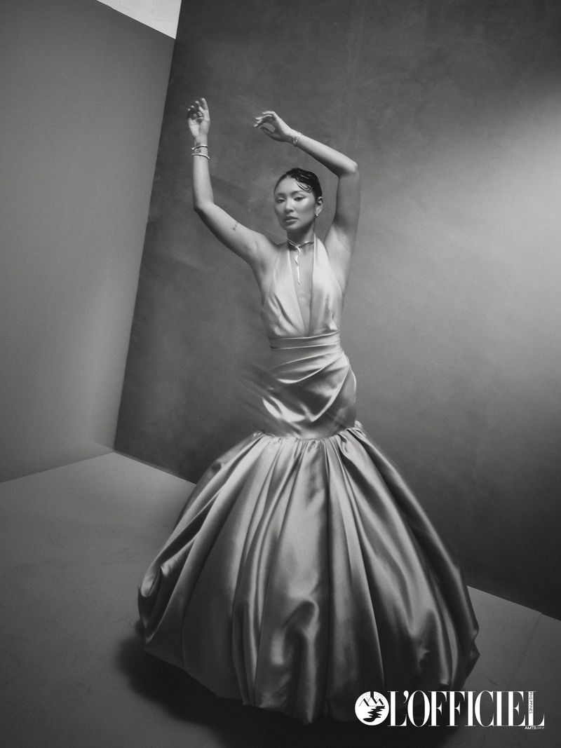 Woman in a voluminous gown posing gracefully with raised arms against a dark studio corner background.