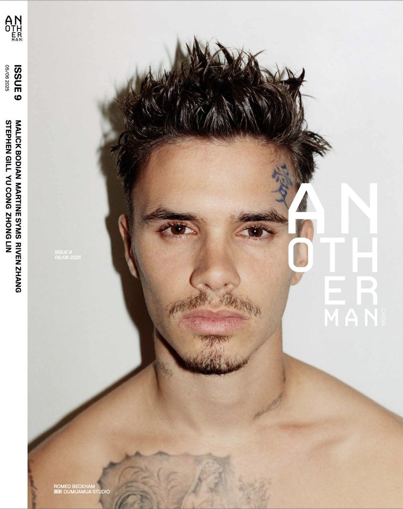 Close-up magazine cover shot of a young man with a goatee and tattoos against a white background, posing for a studio portrait.