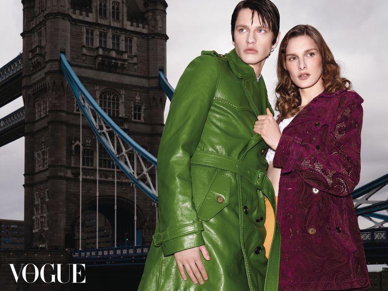 Man in green leather coat and woman in patterned burgundy coat posing before Tower Bridge for Vogue Hong Kong.
