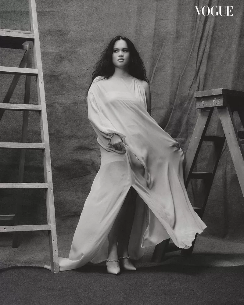 Woman in flowing white gown posing between two wooden ladders for Vogue Philippines Make A Scene editorial